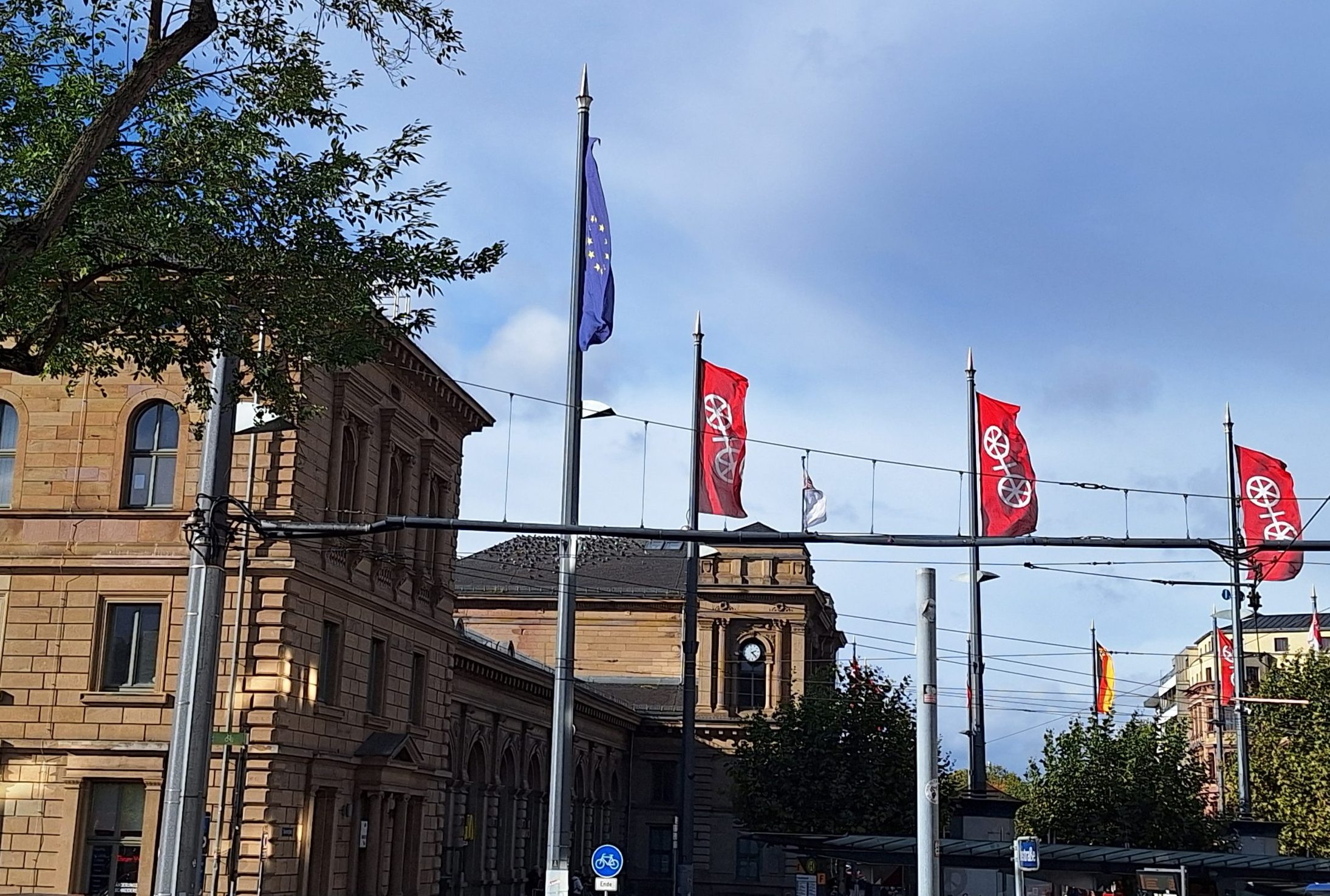 Vor dem Mainzer Hauptbahnhof fliegen mehrere Stadtflaggen, außerdem eine Europaflagge.