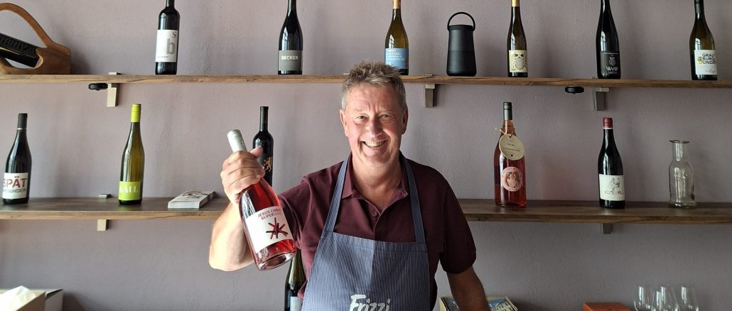 Axel Krüger in blauer Schürze vor seinem Weinregal