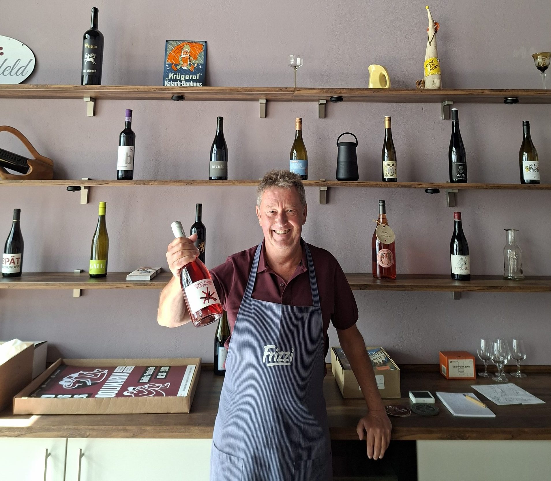 Axel Krüger in blauer Schürze vor seinem Weinregal