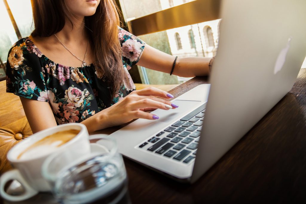 Eine junge Frau sitzt in einem Café und tippt mit ihrer Hand auf das Touchpad ihres Laptops. (Foto: Pexels/Pixabay)
